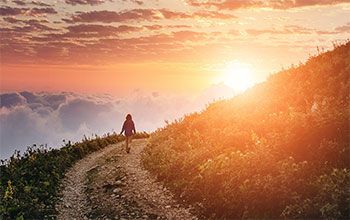 Person walking on mountaintop trail above cloud level at sunset