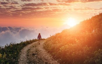 Personne marchant sur un sentier au sommet d’une montagne, au-dessus des nuages, au coucher du soleil