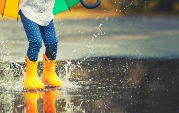 Child wearing yellow rubber boots jumping in puddle